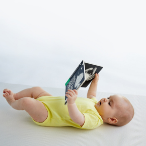 baby laying on back with book