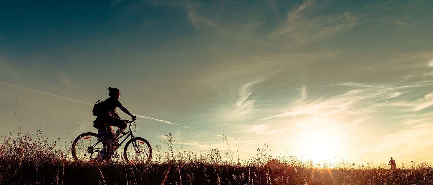 person riding a bike through a field at sunset